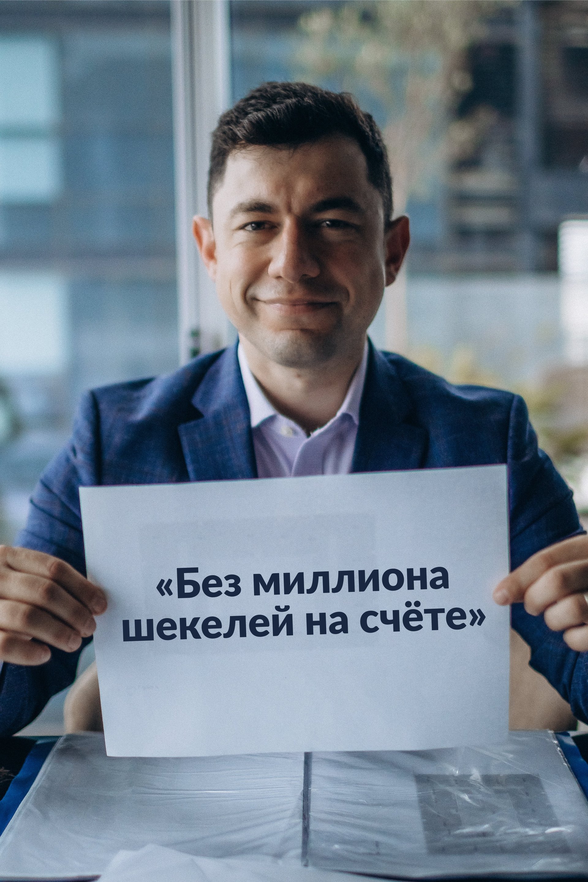 Man in blue blazer holding sign with Russian text in modern office with city view